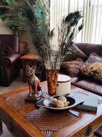 Tropical "Tommy Bahama" style square coffee table. Peacock feathers in vase. Large wood bowl with decorative bowls. Wood cat statue. Decorative animal print decor throw pillows