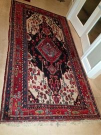A rectangular, polychromatic,
geometric and floral patterned
Persian wool rug with roughly
70 knots per square inch in
shades of red, orange, green,
blue, violet black and white. The
piece is 110 inches long and
60 inches wide.