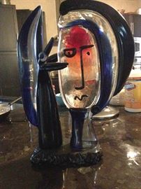 Murano-style glass sculpture
after Pablo Picasso depicting
a primitively created human
face beside a black hand in
shades of red and cobalt. The
piece is 17.25 inches high,
8.25 inches wide and 5 inches
deep.