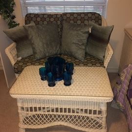 White wicker settee with teal & brown cushions; white wicker coffee table; blue glass pitcher and glasses set