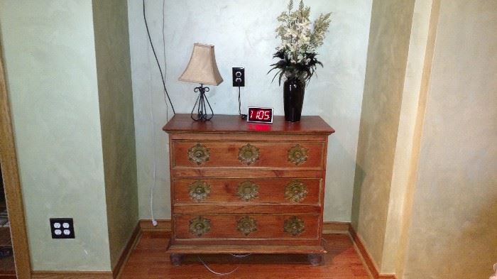 Dresser, lamp, vase with flowers and alarm clock