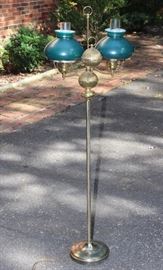 Vintage Floor Lamp

Kept for decades in this fine, non-smoking home. Features a student lamp design, two parallel lights held out by arms on either side. The stand is 55 1/2"T with textured, decorative bulbs. The lights are covered by green glass shades, and within the lightbulb is held by a hurricane shade. Slight chipping on top rims of the green glass shades. Tested and working. 