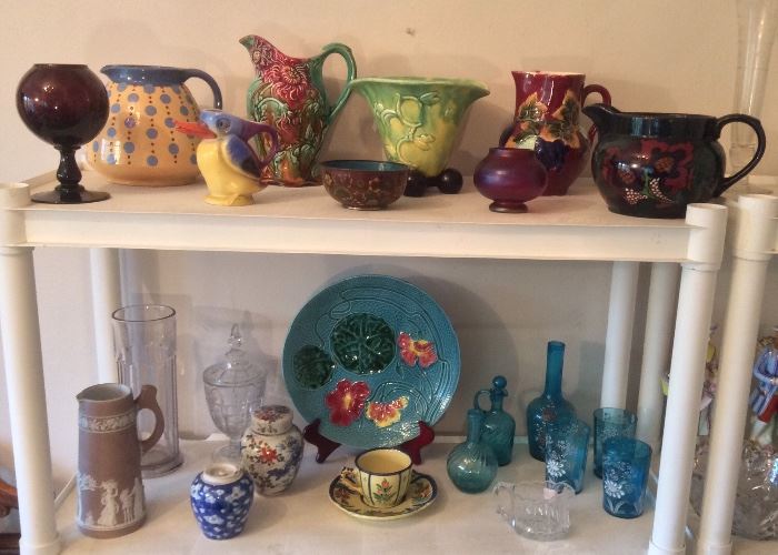 "France P.V." purple glass vase, French ceramic polka dot pitcher, Frie Onnaing majolica pitcher (also French), German bird pitcher, Chinese cloisonne bowl, interesting yellow & green vase, Czech majolica pitcher, small pink iridescent vase, Decoro pitcher (England). Bottom row: Pink Wedgwood Jasperware pitcher, ginger jars, turquoise majolica plate, Quimper cup & saucer, blue glass bottles, decorated blue glass decanter & tumblers.