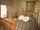 Queen bed with four posts and acorn finials and bedding. Wall tapestry.