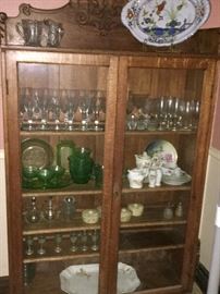 This glass-footed oak China hutch features an Austrian porcelain set, green uranium glassware and dishes, crystal glassware and porcelain platters.