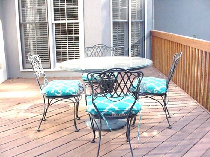 Wrought iron patio set, glass top table and four chairs with cushions