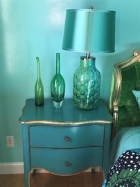 Glass deco, much of it signed, aqua lamps and two antique, painted two-drawer side tables with gold leaf.