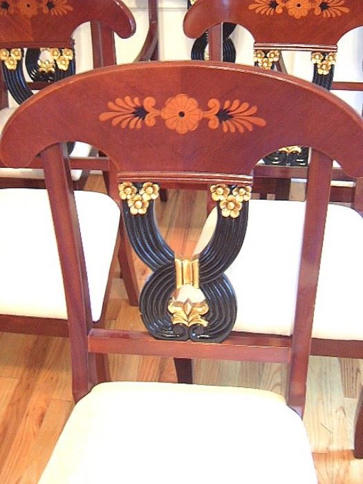 Close up of wood inlay, & gilt & black center back rest on set of dining room chairs.