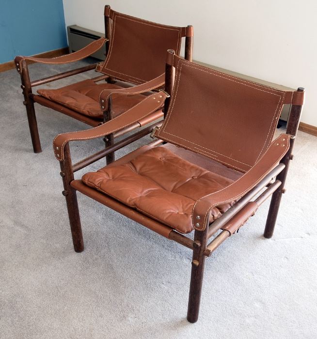 A pair of Arne Norell Safari chairs with slung leather arms and a rosewood frame.