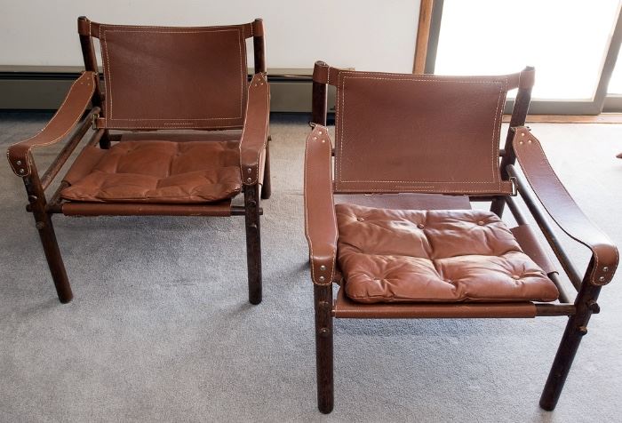 A pair of Arne Norell Safari chairs with slung leather arms and a rosewood frame.