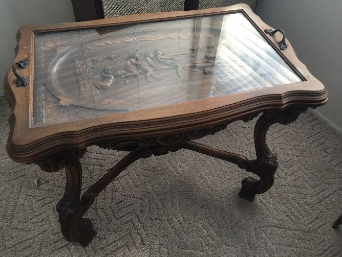 Highly carved antique table with removable tray top with glass insert.  Solid wood.  Carved motif features children on tree branch.  Elaborately carved legs