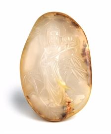 48. JADE CARVED GUAN YIIN PEBBLE白玉把件Skillfully carved to be framed within the natural dark inclusions, the center of this jade pebble depicts a serene Guan Yin holding a lotus blossom among bamboo trees. 95g L: 3in W: 2in