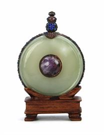 65. ROUND JADE ENAMEL SNUFF BOTTLE玉胎景泰藍鼻煙壺With cloisonne edges and stopper, this flattened circular snuff body has a jade body punctuated by a purple stone. H:3 1/2in 84g WITH STAND