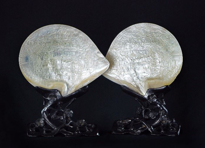 74. PAIR OF SHELL CARVINGS ON WOOD STANDS貝殼雕人物故事擺件一對Identical mother-of-pearl shells intricately carved to the interior with warriors and government officials in a courtyard setting, with lotus blossoms meandering below, on top of stands carved from dark wood with openwork branches and blossoms.H: 11 1/2 in   W: 9 in