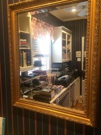 Lots of electronics and office supplies are reflected in the gold framed mirror.