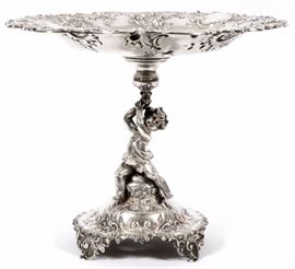 Lot#1034, AUSTRIAN .800 SILVER FIGURAL COMPOTE, H 10", DIA 12"An Austrian .800 silver figural compote. Circa 1872-1922. Probably by Rothe & Neffe, Vienna. The figural standard in the form of a putti supporting a bulbous stem, surmounted by a large detailed floral and foliate Rococo scrolled circular top, the whole raised on a foliate Rococo-scrolled base ending in scrolling feet. Height 10", dia. 12". 32.50 troy ounces.