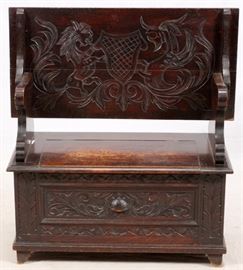 Lot#1074, CARVED OAK MONK'S BENCH, 19TH C., H 29", W 17 1/2", L 36"The flip-over rectangular top carved with a lion and dolphin heraldic design, above shaped armrests and hinged opening storage seat, the façade with foliate and scroll motif.