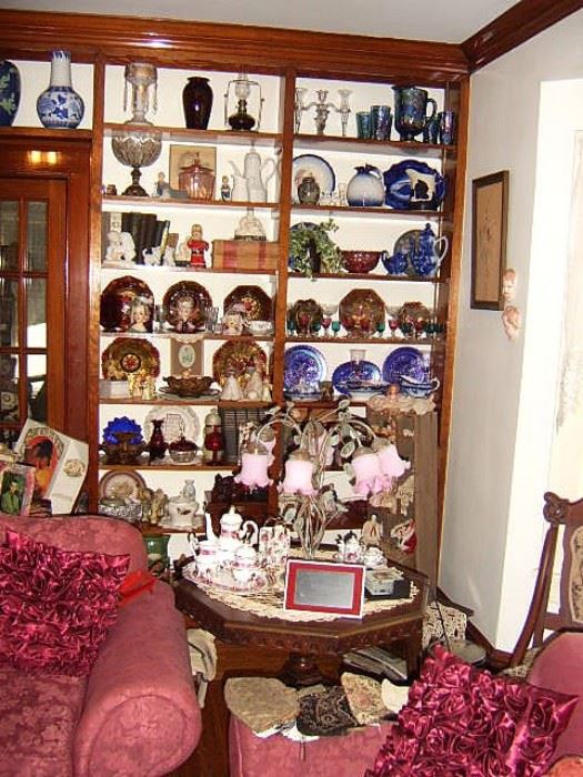 Victorian lamp, pedestal table, and antique glass & china on shelves.