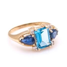 14K Yellow Gold Topaz, Sapphire, and Diamond Ring: A 14K yellow gold topaz, sapphire, and diamond ring. This ring features a smooth shank leading to sapphire and diamond encrusted shoulders on either side of a prong set topaz stone.