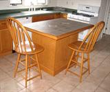 Oak kitchen center island with tile top with two chairs.