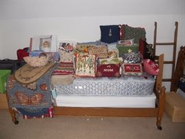 One of a set of maple twin beds holding lots of decorative pillows and rugs
