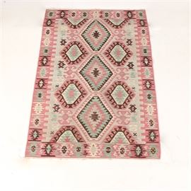 Turkish Handwoven Flatweave Kilim Rug: A Turkish handwoven flatweave kilim rug. This kilim handwoven rug has three center medallions and is anchored by groupings of geometric symbols along the sides. Constructed with a flatweave, it features pinks, grays, turquoise, bold browns, and alternating patterns of geometric symbols on the border.
