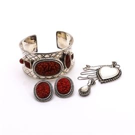 Sterling Silver Mother of Pearl, Marcasite, and Coral Jewelry: A collection of sterling silver mother of pearl, marcasite, and coral jewelry. This collection features a pair of clip on oval rope earrings with floral carved coral centers, a matching cuff bracelet housing bezel set carved coral stones, a heart pendant encrusted with marcasite stones and housing a bezel set mother of pearl center, and a spring ring clasp connected to a box chain necklace leading to a pear shaped pendant encrusted with marcasite stones and a bezel set mother of pearl center. Imprinted upon each piece is “925.” The total approximate weight of this collection, inclusive of non-metal materials, is 3.51 ozt.