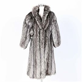 Yves Saint Laurent Fox Fur Coat: A Yves Saint Laurent fox fur coat. This silver tone fur coat features a wide collar and a black interior lining. The original manufacturer tag reading “Furs Alixaudre New York” and “Yves Saint Laurent” is present to the interior.