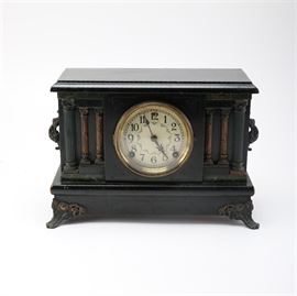 Sessions Clock Co. Mantle Clock: A Sessions Clock Co. mantel clock. It is in a victorian style with a flat top and column design along the front on either side of the clock face. The piece has metal hardware and four small feet at each corner.