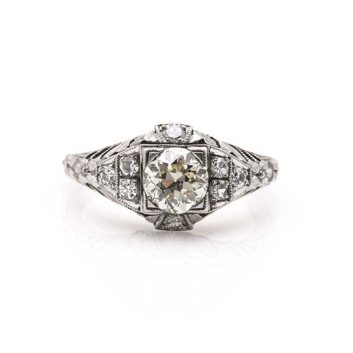 Platinum and Diamond Ring: A platinum and diamond ring. This ring features a decorative textured shank leading to ornate open work shoulders on either side of the diamond-encrusted center housing a diamond center stone with eight diamond side stones; the total approximate item weight is 2.90 dwt.