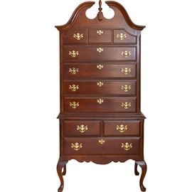 Queen Anne Style Contemporary Highboy: A Queen Anne style highboy. This contemporary piece features a broken swan neck pediment with central finial, five drawers in the top case and three drawers below, all with brass bail pulls. The cabriole legs terminate in pad feet. This piece is part of a matching bedroom set purchased at Levitz Furniture. Coordinating pieces in items 17WDC023-040, 17WDC023-041, and 17WDC023-043. Located on the second floor.