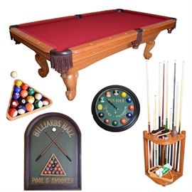 Billiards Table and Accessories: A billiards table with cover and accessories. This table features a red felt covered slate top, fringed leather web pockets, and a wheat colored wood frame on scrolled feet. Includes ten cues, a cue rack, a complete set of balls with triangle rack, a 9-ball rack, a repair kit for re-tipping cues, chalk, table brush and rail brushes, a “Billiards Hall” decorative wall hanging, and a “Fox Glen Tavern Billiards” wall clock with billiard balls as the hour markers.