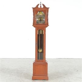 Cherry Grandfather Clock by Emperor: A grandfather clock by Emperor, made in Germany, constructed of a cherry wood case. This clock features a broken pediment, turned details, and brass-toned hardware, as well as a turning sun and moon design on its face.