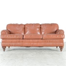 Saddle Tan Leather Sofa: A saddle tan leather sofa. The three cushion sofa has rolled arms, dark wood bun feet, and removable seat cushions.