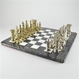 Marble Chess Board with Cast Metal Pieces: A black and white marble chess board with cast metal pieces. The pieces are modeled to represent fantasy-style members of the royal court. They are finished in gold and silver tones.