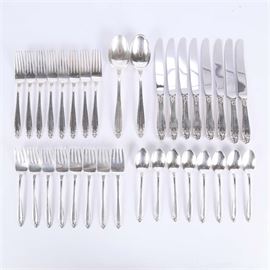 "Prelude" International Sterling Silver Flatware: A set of “Prelude” international sterling silver flatware. The set includes eight knives, eight dinner forks, eight salad forks, eight spoons, and two large serving spoons. The knives have stainless steel blades. The pattern is designed by Alfred G. Kintz and features a scalloped tip and garland design. The total weight of the set is 34.707 ozt, exclusive of knives.