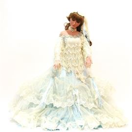 33" Rustie Porcelain Doll: A 33" Rustie porcelain doll. This doll features long light brown curly hair with thick bangs and blue eyes. The doll is dressed in a floor-length light blue gown with tulle, layered white lace, and white cream colored beaded tassels to the top. The back of her neck is marked “Rustie, © 2001, # 251/300”.