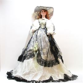 Cathay Collection Porcelain Doll: A Cathay Collection porcelain doll. The doll has auburn hair and wears a black, grey and white dress with puff sleeves and a scalloped hem overskirt with lace trim and a coordinating hat. The doll is numbered “1-5000” and stamped “Cathay Collection” at the back of the neck.