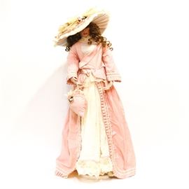 Pat Dezinski Porcelain Doll: A signed and numbered collectible Victorian style porcelain doll by Pat Dezinski. The doll has curly brown hair, and is wearing a pink and white dress, matching hat and purse, with realistic bloomer and petticoat undergarments and laced boots. The doll is hand signed and hand numbered “2003, 149/400” to the back at the neck base. A stand is included.