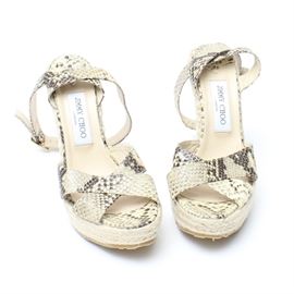 Jimmy Choo Wedge Heels: A pair of wedge style heeled shoes by Jimmy Choo. These shoes have a braided jute heel and snakeskin leather straps across the top of the foot and around the ankle. The ankle straps cross around the leg twice and have a metal buckle. The shoes have a rubber sole and are a size 39.