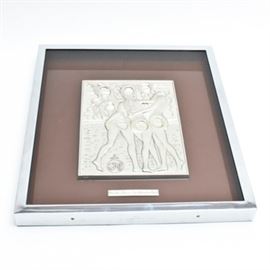 Framed Sculpture in Silver After Salvador Dalí's "Las Tres Gracias": A silver sculpture after surrealist artist Salvador Dalí (1904-1989) work titled Las Tres Gracias. This bas relief work is rendered in sterling silver and depicts three standing female figures each with egg shaped holes in their bodies. The sculpture is signed to the lower left corner. The work has been framed behind glass in a silver metal shadow box frame that also has a brown tinted glass backside. Within the frame is also a metal marker reading, “Las Tres Gracias por Salvador Dalí”. On the reverse is a certificate of “uniqueness and authenticity” detailing this work as specimen number 678.