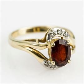 14K Yellow Gold, Garnet, and Diamond Bypass Ring: A 14K yellow gold ring featuring one center faceted oval garnet accented by surface prong set diamonds, mounted on a split bypass style shank.