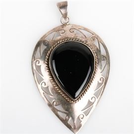 Onyx and Sterling Silver Openwork Pendant: A teardrop shaped sterling silver pendant featuring a center bezel set onyx pear shaped cabochon with a braided border mounted on a scrolling openwork frame with a tapered bail.