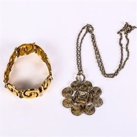 Metropolitan Museum of Art Jewelry: An assortment of Metropolitan Museum of Art jewelry. Includes a 7.5" gold tone Mughal twin fish bracelet with a box clasp marked “MMA” and a silver tone pendant necklace. The pendant features numerous swirl shapes clustered together and hangs on a 23" textured link chain. It is marked " © The Metropolitan Museum of Art".