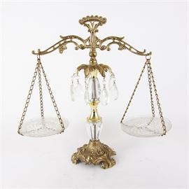 Decorative Brass and Glass Apothecary Scale: A decorative apothecary balance scale. This piece has an ornate brass frame featuring glass pans, hanging prisms, and stem accents. The scale rests on a footed base.