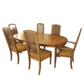Foster-McDavid Furniture Dining Table and Chairs: A Mid Century dining table and six chairs by Foster-McDavid Furniture, Inc. of Tampa, Florida. Each piece has a wooden frame with a walnut finish. The table has an oval top that rests on four tapered legs and comes with an extra leaf. The chairs feature caned backrests, padded seats covered in mustard yellow fabric, tapered front legs, curved back legs, and maker’s tags on the undersides, and they include two captain’s chairs.