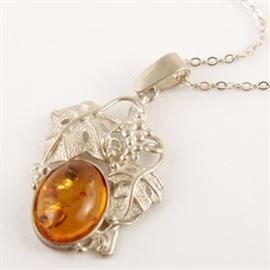 Sterling Silver and Amber Openwork Pendant Necklace: A sterling silver pendant necklace featuring a foliate openwork pendant accented by a bezel set amber cabochon. It hangs on a link chain with a spring ring clasp.