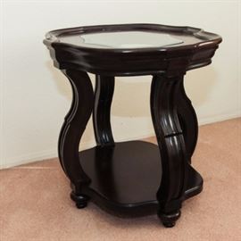 Wood and Glass Accent Table: An accent table. This piece has a wooden frame with a dark brown finish, and it features a shaped top with raised lip and a center panel of glass. The table rests on four curved legs with a shelf stretcher and turned bun feet.