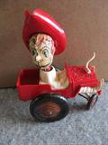 A 6" by 7" lithographed tin cowboy in a red metal car. He has a white plastic "suit" and a red plastic hat. He moves great, and he is just missing one steer horn.