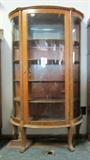 Antique oak bow front china cupboard, with bow feet and mirrored top shelf.  In nice condition, with original key (glass on lower right side has crack).  Approx. 63H x 37W x 16D.